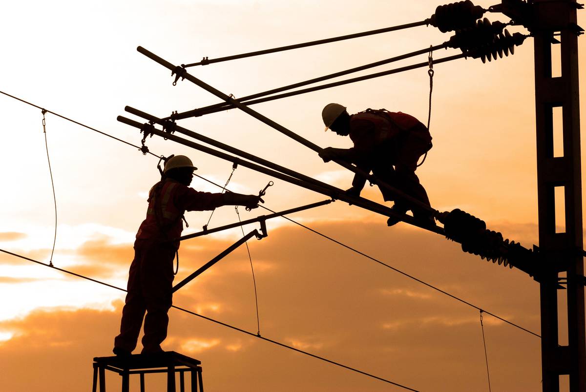 Electricians working on overhead power lines at sunset